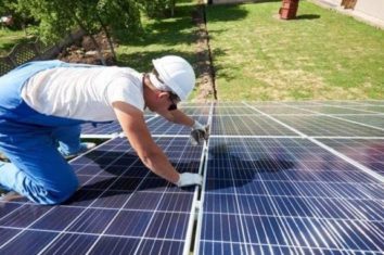 安装全新的太阳能电池板的房子的屋顶的人